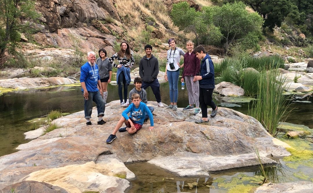 Group of students on rock in river, with teacher